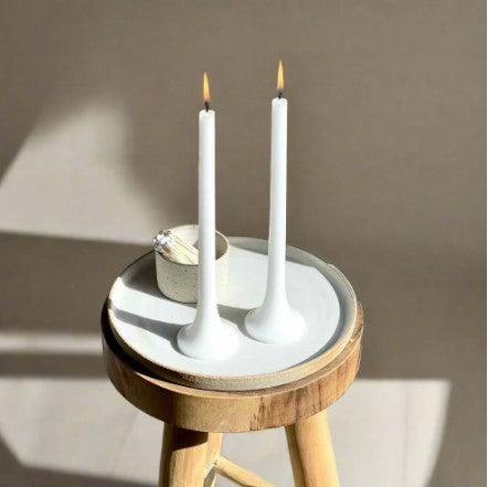 Two white candles on a small round wooden stool with a neutral background
