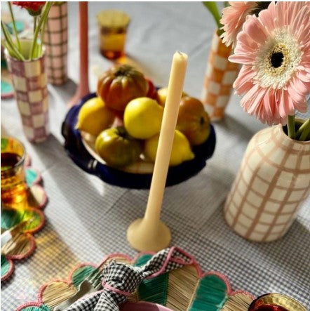 Decorative table setting with fruits, flowers, and candles on a checkered tablecloth.