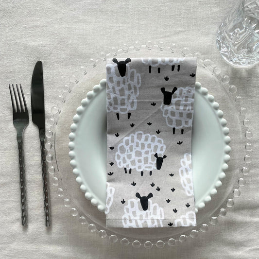 Table setting with sheep-themed napkin, plates, and cutlery on a textured surface.