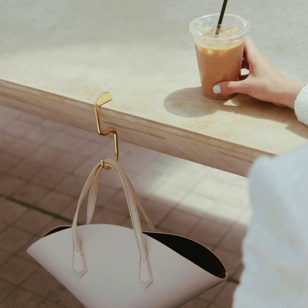 Hand holding a cup of iced coffee next to a handbag on a wooden surface.
