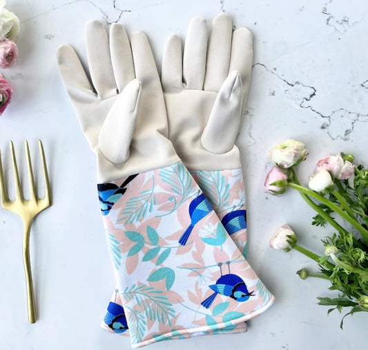Gardening gloves with floral and bird pattern on a marble surface with flowers and a fork.