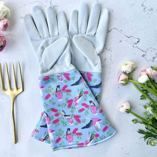 Gardening gloves with floral pattern on a marble surface with flowers and a fork.