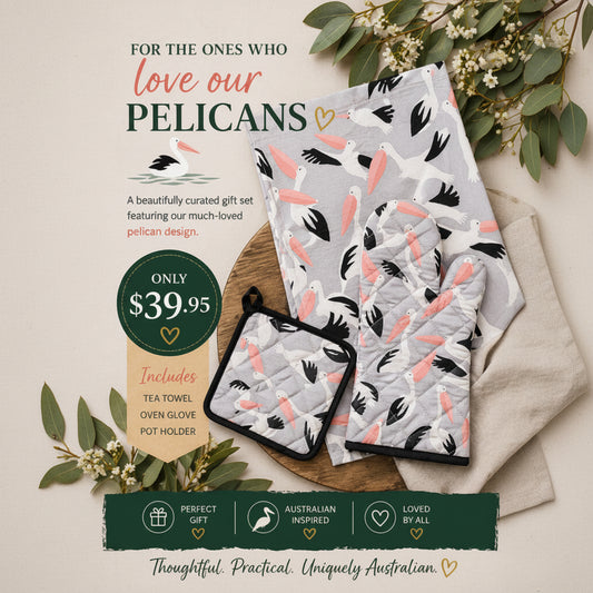 Gift set with pelican design towels, pot holder, and oven glove on a wooden board with greenery.