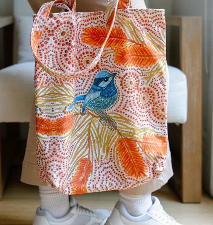 Tote bag with leaf and bird pattern held by a person wearing white sneakers.