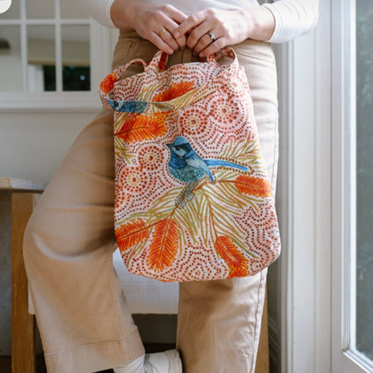 Person holding a colorful bag with a bird design in an indoor setting