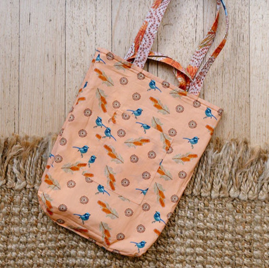 Peach-colored tote bag with bird pattern on a wooden surface