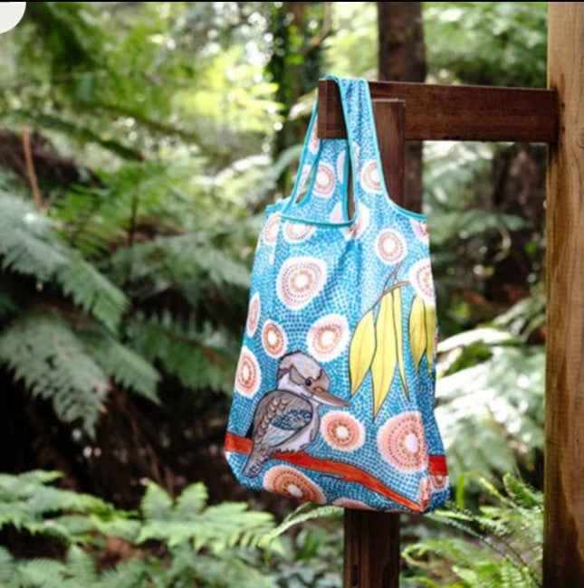 Reusable shopping bag with floral and bird design hanging on a wooden post in a forest setting