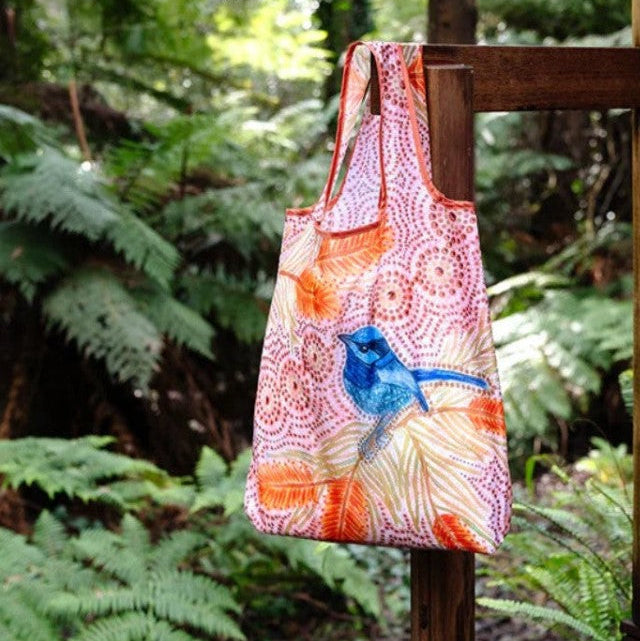 Colorful tote bag with bird design hanging on a wooden post in a forest setting