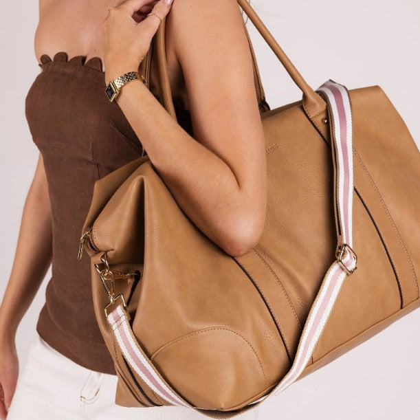 Brown leather bag with a strap held by a person against a neutral background
