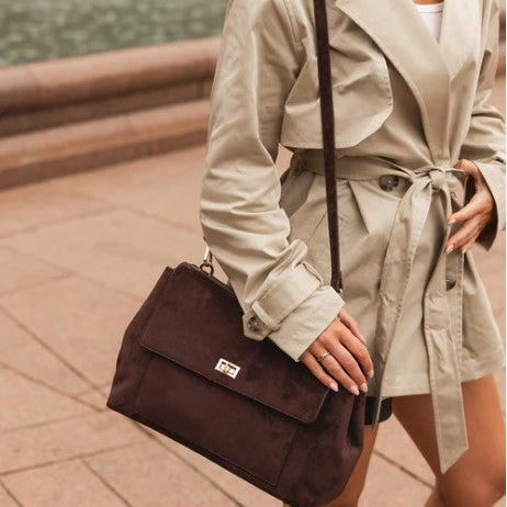Person wearing a beige trench coat holding a brown handbag outdoors.