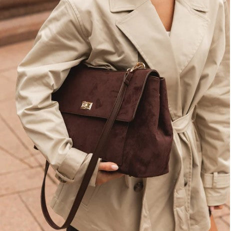 Person holding a brown bag with a beige trench coat