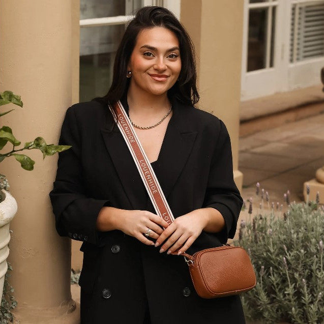 Woman in black outfit with brown sash and bag standing outdoors.