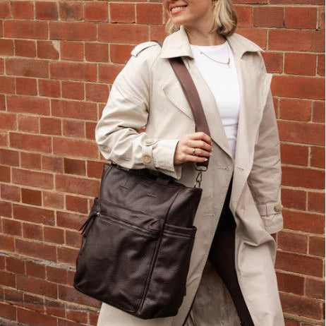 Woman holding a brown leather bag against a brick wall