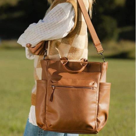 Brown leather bag held by a person in a field