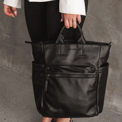 Person holding a black leather bag against a gray background