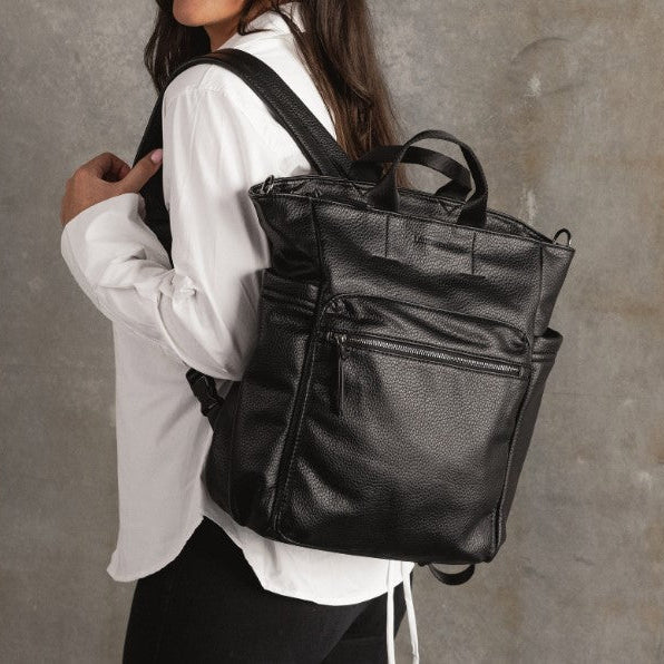 Person wearing a black leather backpack against a neutral background