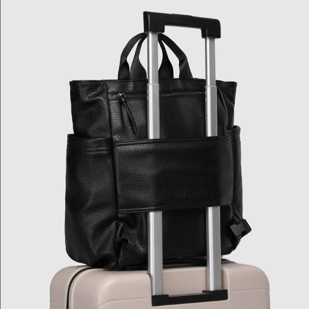 Black leather bag with a handle on top of a beige suitcase