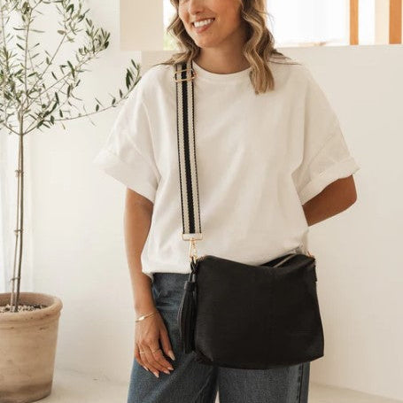 Woman holding a black bag indoors with a plant in the background