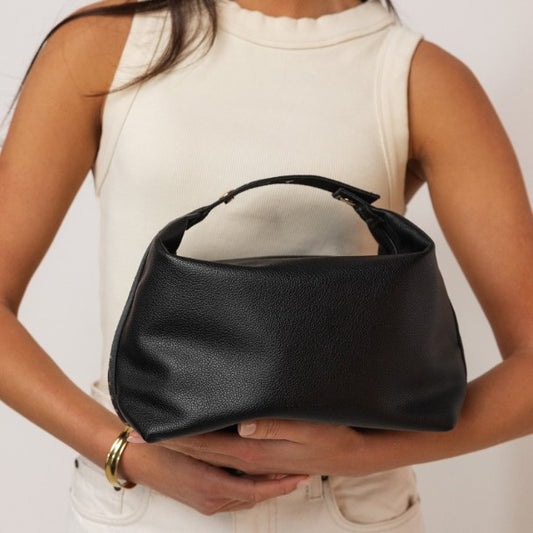 Person holding a black bag against a neutral background