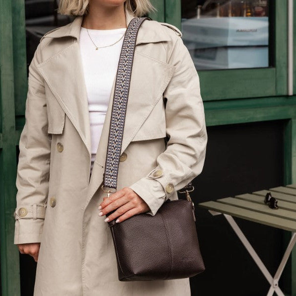 Person wearing a beige trench coat holding a brown bag.