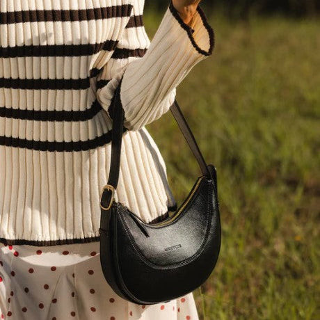 Person holding a black handbag with a blurred grassy background