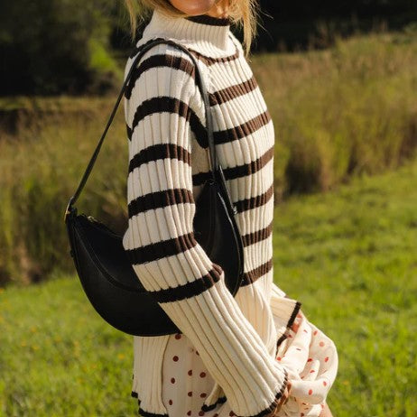 Person wearing a black and white striped sweater with a black bag in a grassy field