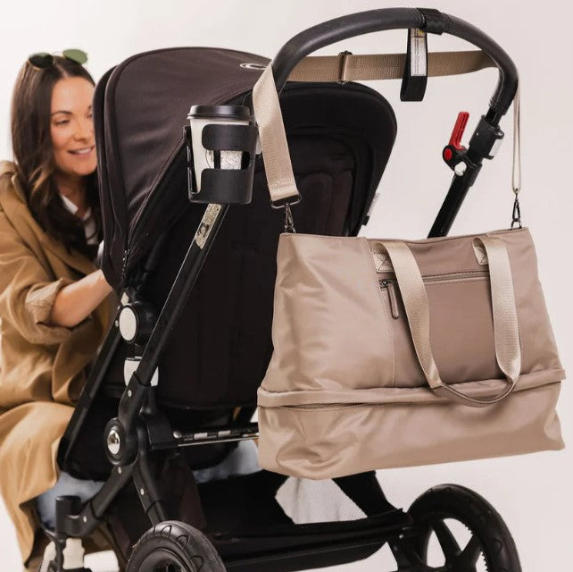 Woman pushing a stroller with a beige bag attached, on a white background