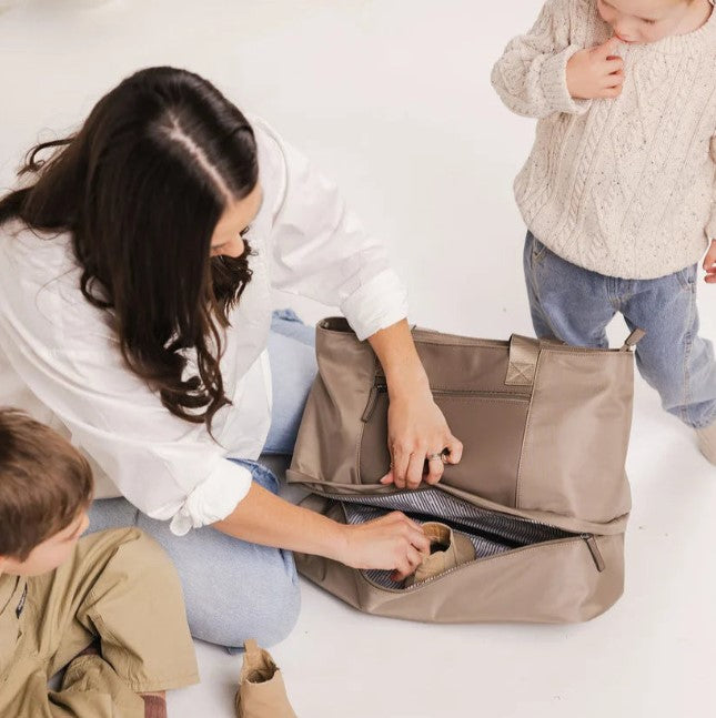 Woman opening a beige bag with two children on a white background