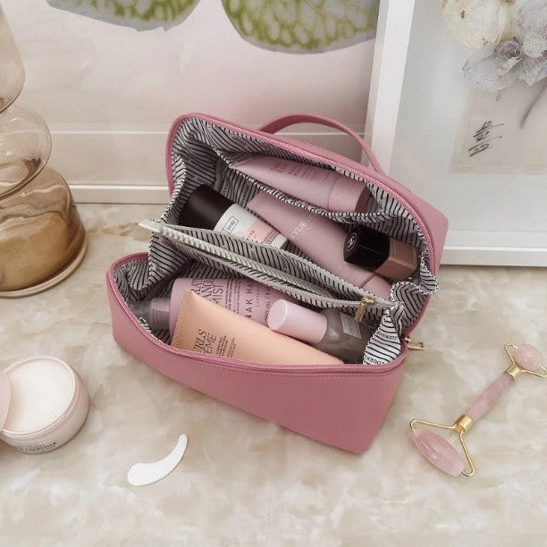 Pink cosmetic bag with skincare products on a marble surface