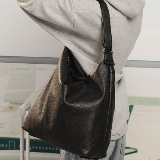 Person wearing a gray hoodie and carrying a black shoulder bag on a blurred indoor background