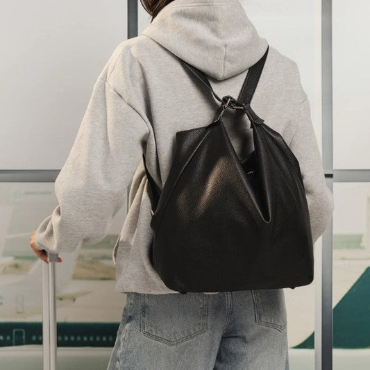 Person wearing a black backpack and holding a suitcase in an indoor setting