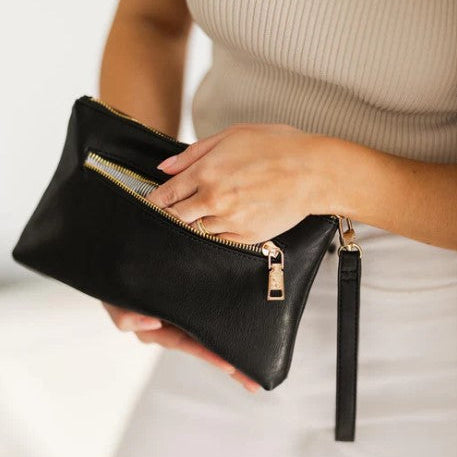 Person holding a black clutch bag with gold zipper and strap.