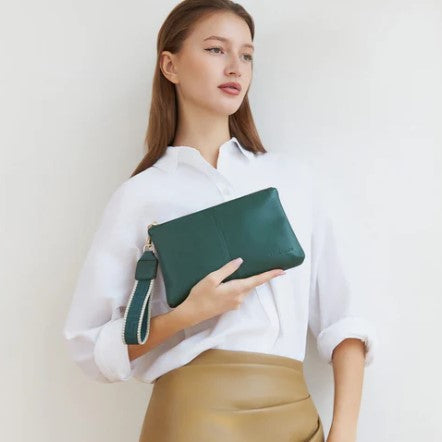Woman holding a green clutch against a plain background