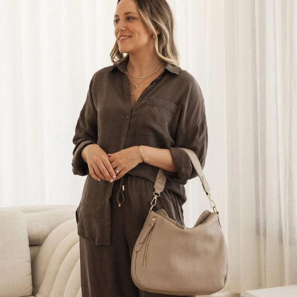 Woman holding a beige handbag in a neutral setting