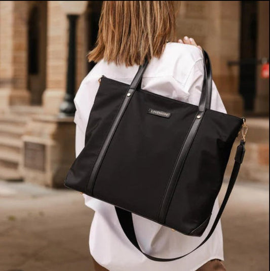Person carrying a black tote bag outdoors