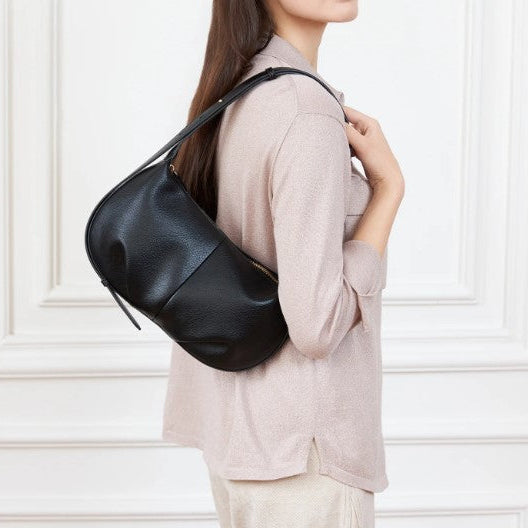 Person wearing a black leather shoulder bag against a white wall