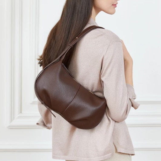 Woman wearing a brown leather shoulder bag against a white wall