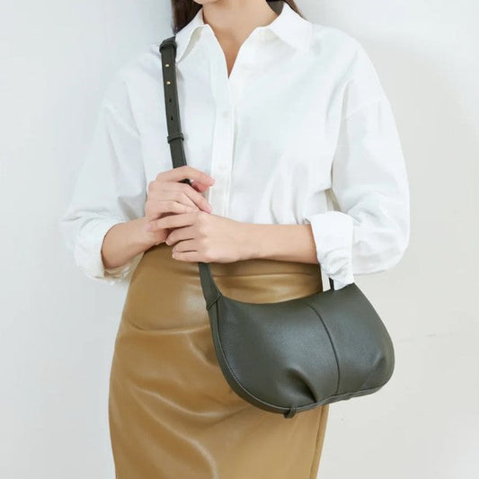 Person holding a green leather bag against a plain background