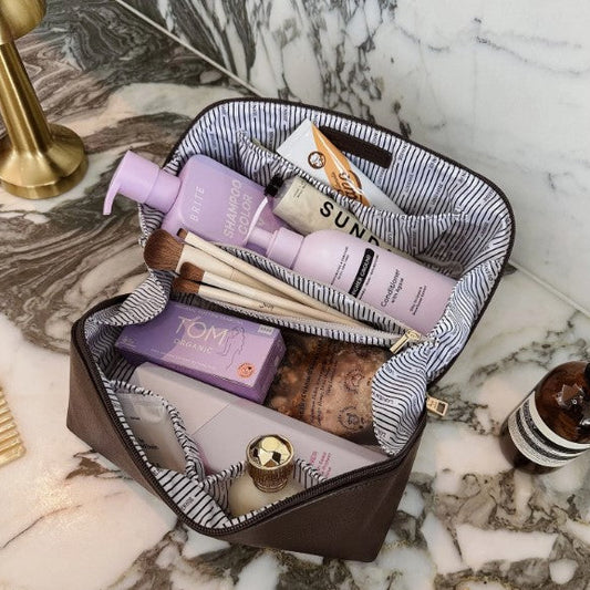 Makeup bag with skincare products and brushes on a marble surface
