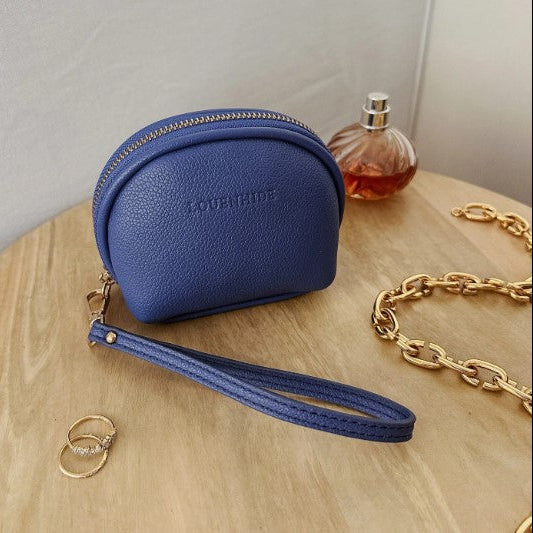 Blue wristlet purse with 'Louenhide' branding on a wooden surface with a bottle of perfume and gold chain.