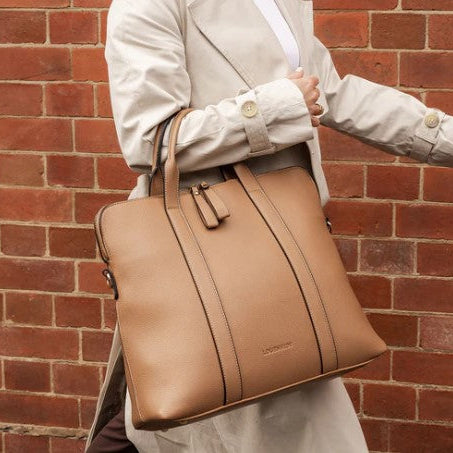 Person holding a tan laptop bag against a brick wall