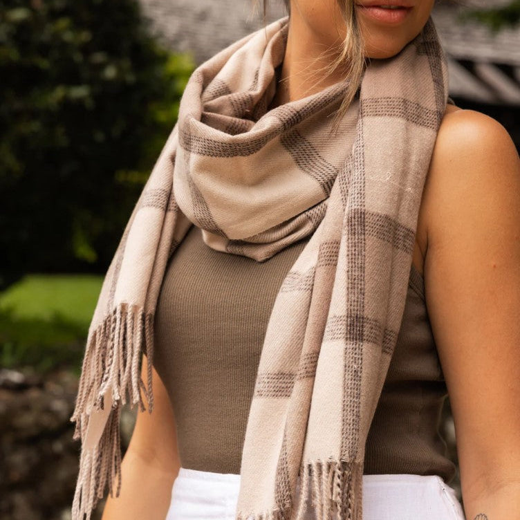Woman wearing a beige plaid scarf with fringe, standing outdoors.