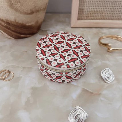 Round jewelry case with red and white pattern on a textured surface with jewelry items.