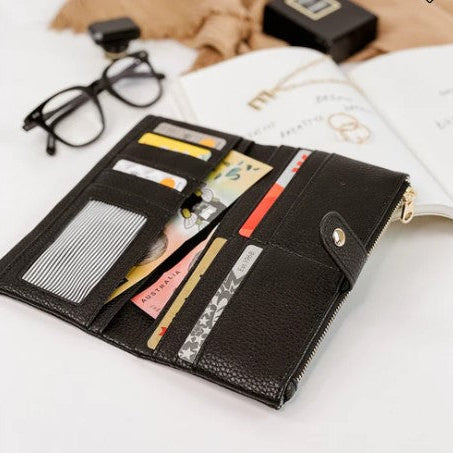Black wallet with multiple cards on a white surface with glasses and a book in the background