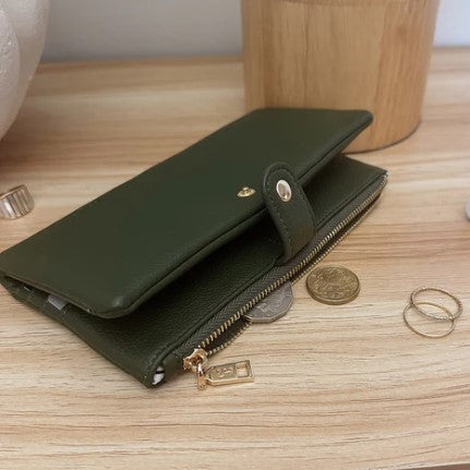 Green wallet with gold zippers on a wooden surface with coins and a ring.