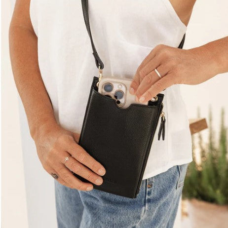 Person holding a black crossbody bag with a phone case inside, wearing a white shirt and blue jeans.