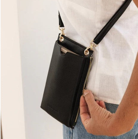 Black crossbody bag with gold zipper held by a person against a light background