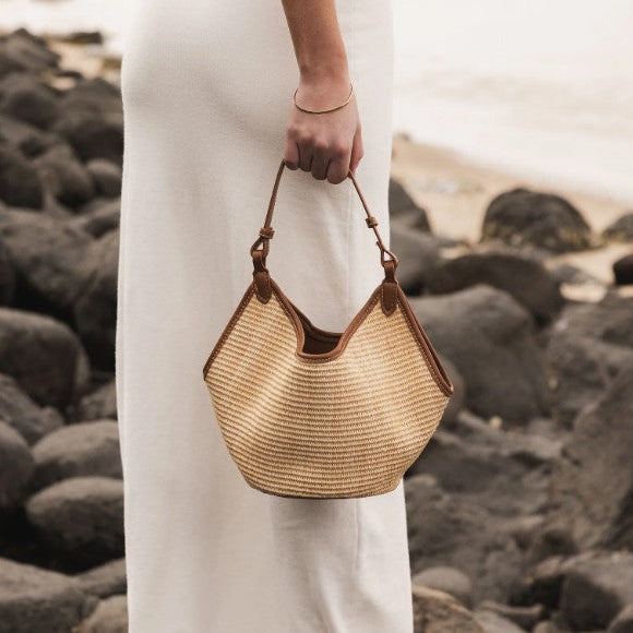 Person holding a woven handbag on a rocky beach