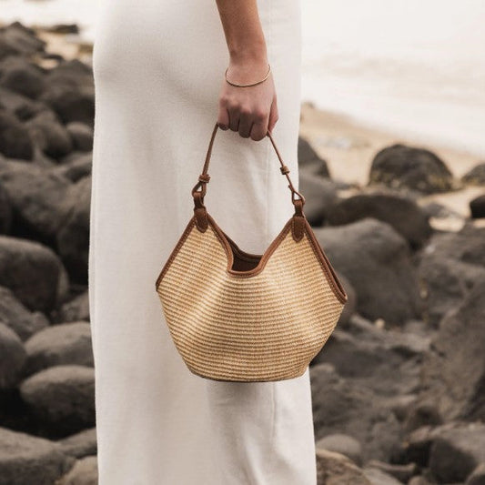 Person holding a woven handbag on a rocky beach
