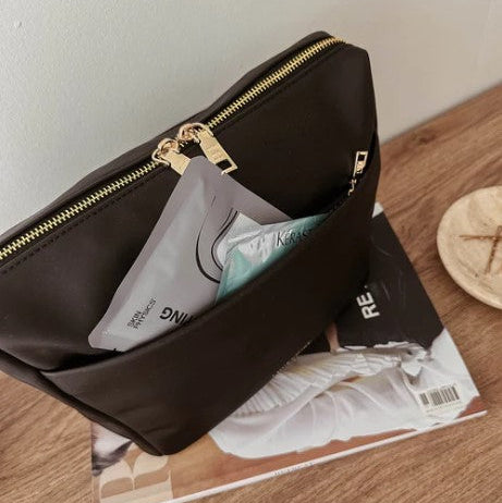 Black cosmetic bag with gold zipper on a magazine